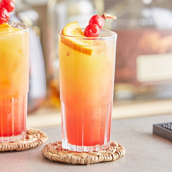 Two Duralex highball glasses filled with orange and cherry cocktails, garnished with cherries.