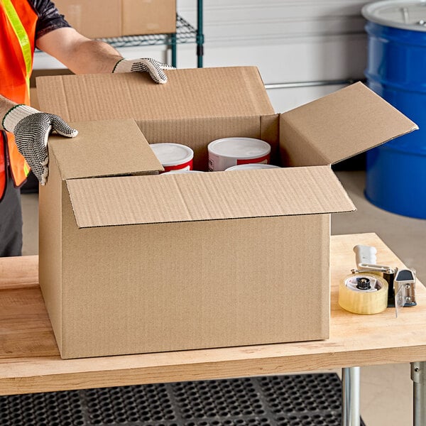 A person wearing gloves opens a Lavex Kraft cardboard box to reveal white containers inside.