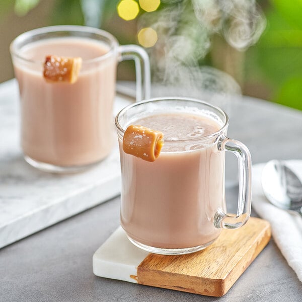 A glass mug of UPOURIA Salted Caramel Hot Chocolate with a caramel on top.