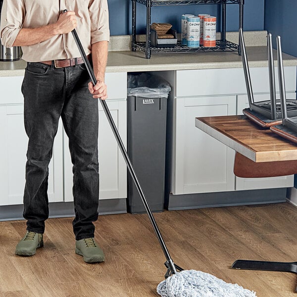 A man using a Lavex Black metal mop handle to mop the floor in a professional kitchen.