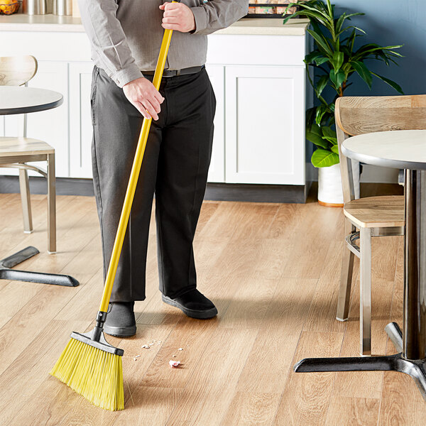 A man sweeping the floor with a Lavex yellow metal broom handle.
