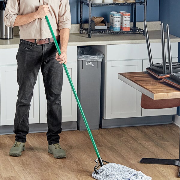 A man using a Lavex metal mop handle to clean the floor in a professional kitchen.