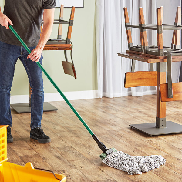 A person using a green Lavex metal mop handle to clean the floor.