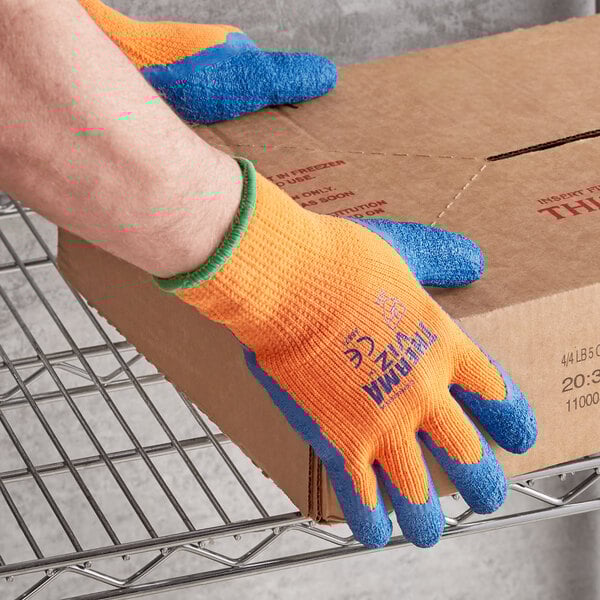 A person wearing Cordova orange terry thermal gloves with blue latex palm coating on a box.