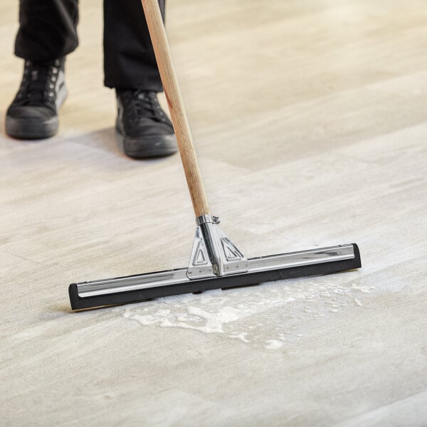 A person using a Lavex black double neoprene foam floor squeegee with metal frame to clean the floor.