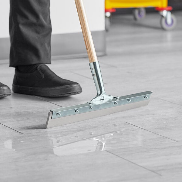 A person using a Lavex rubber floor squeegee to clean the floor.