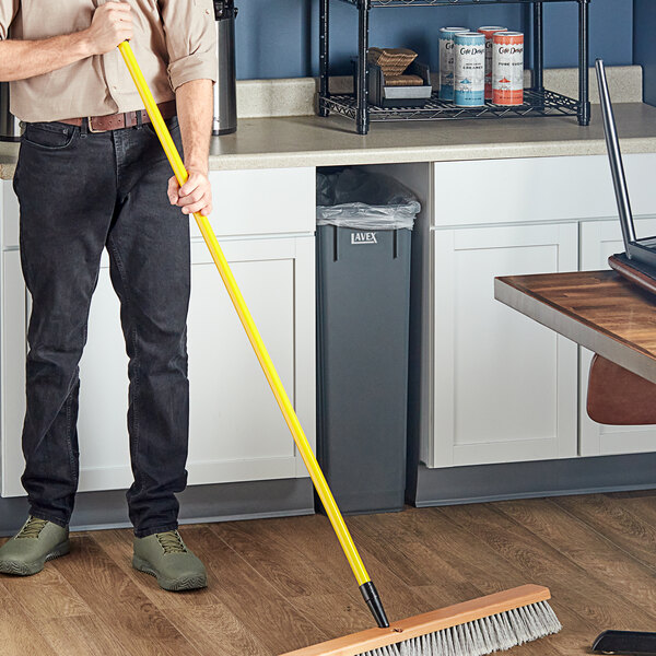 A man sweeping the floor with a yellow Lavex threaded fiberglass broom handle.