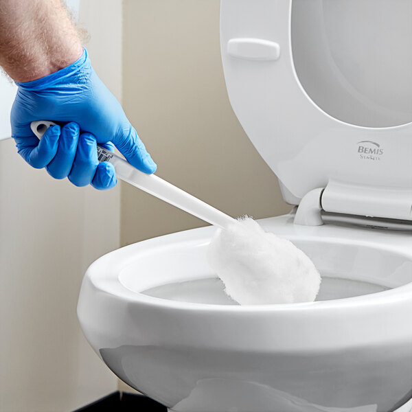 A person in blue gloves cleaning a toilet with a Lavex white acrylic yarn toilet bowl brush.