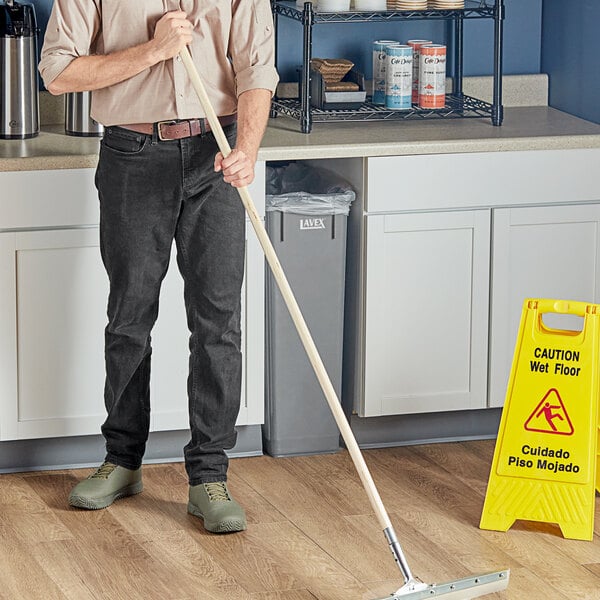 A man standing in a hospital cafeteria holding a Lavex threaded wood broom handle.