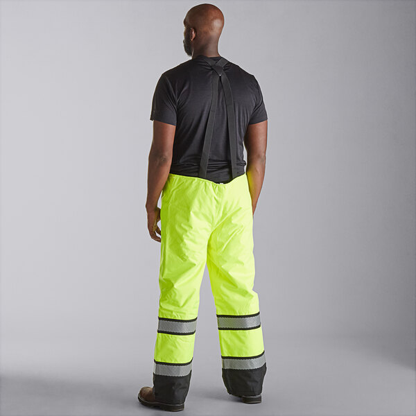 A man wearing Cordova Hi-Vis lime yellow quilted bib pants over a black shirt.