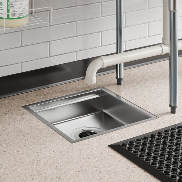 A square 18-inch by 18-inch stainless steel floor sink installed in a commercial kitchen floor.