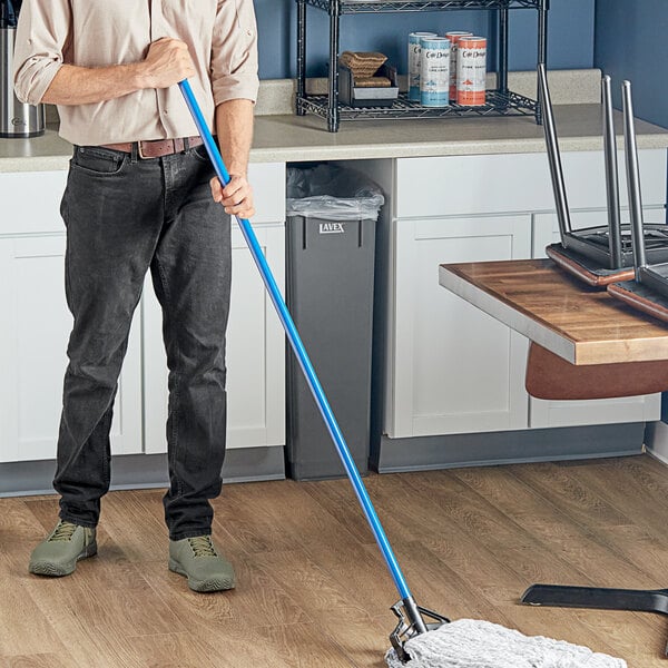 A man using a Lavex blue metal mop handle to mop the floor in a professional kitchen.