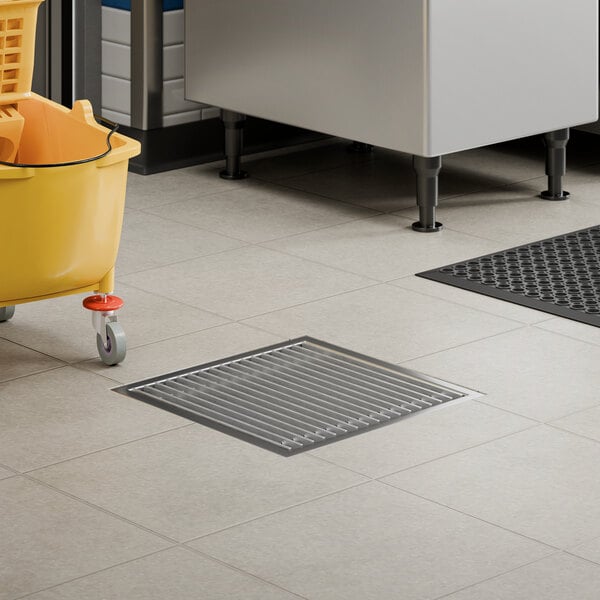 An 18-inch by 18-inch stainless steel floor sink with a removable grate installed in a tiled floor.