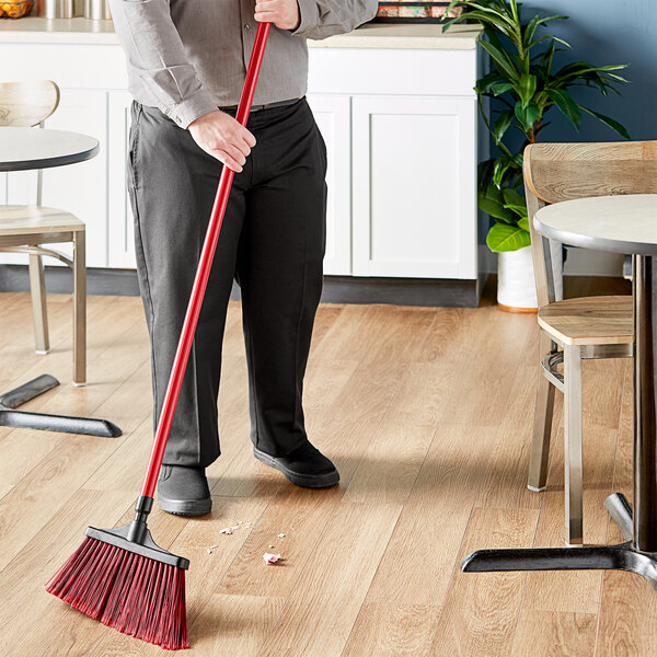 A person using a Lavex red fiberglass broom handle to sweep the floor in a corporate office cafeteria.