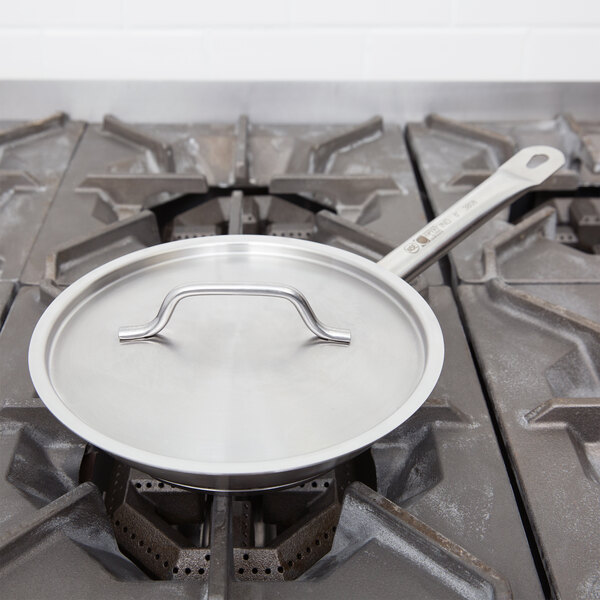 A Vollrath stainless steel pan cover on a pan over a gas stove.