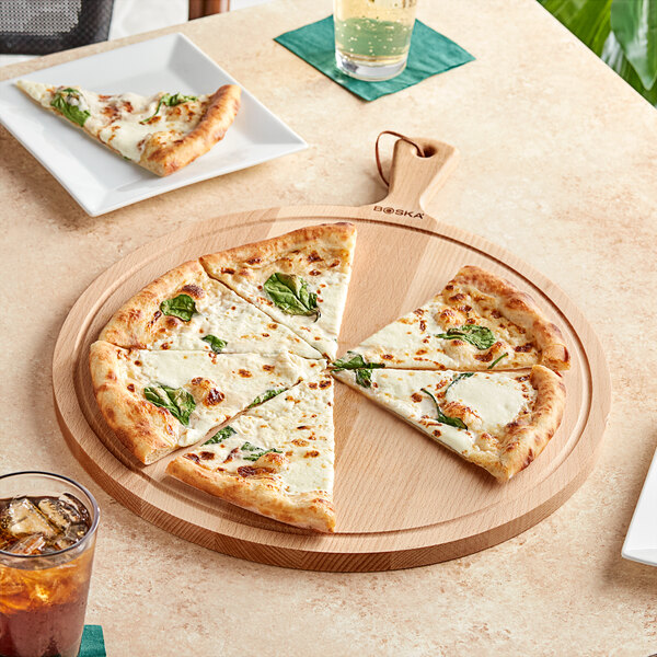 A slice of pizza with cheese and basil on a Boska round beech wood serving board.