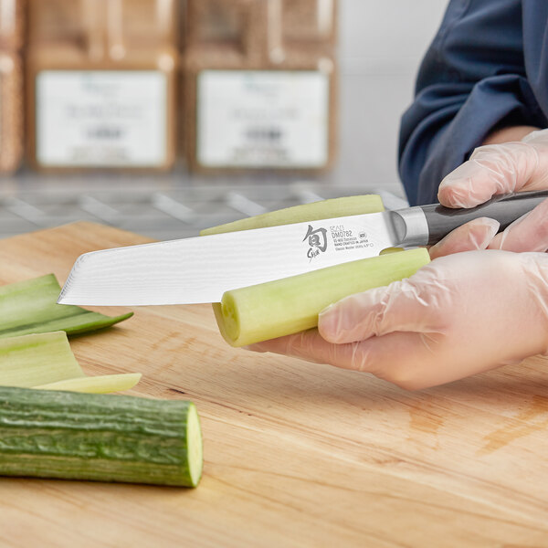 A person in gloves using a Shun Classic forged utility knife to cut vegetables.