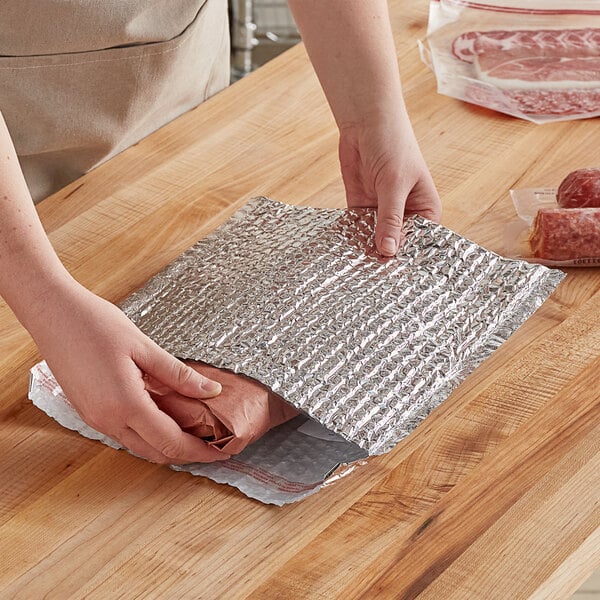 A person wrapping a piece of meat in a Lavex insulated foil bubble mailer.