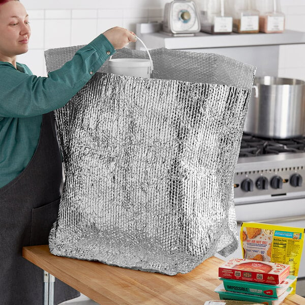 A woman pouring liquid into a large silver foil bag in a professional kitchen.