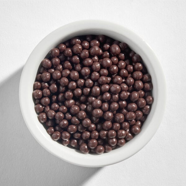 A white bowl filled with small, round Callebaut dark chocolate crispearls.