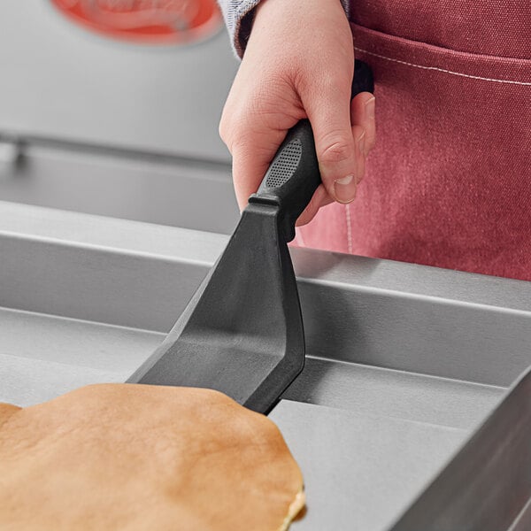 A hand holding a black Fourt&#233; high heat nylon solid turner flipping a pancake.