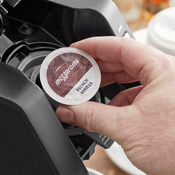 A hand holding a round white and brown label on a box of Ellis French Vanilla Brulee Coffee Single Serve Cups.