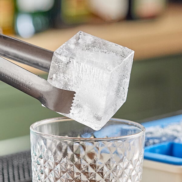 A person using tongs to put a large blue OXO Good Grips ice cube in a glass.