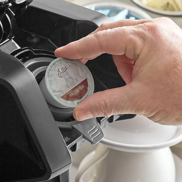 A hand holding a round white and red label for Ellis William Penn Coffee Single Serve Cups.