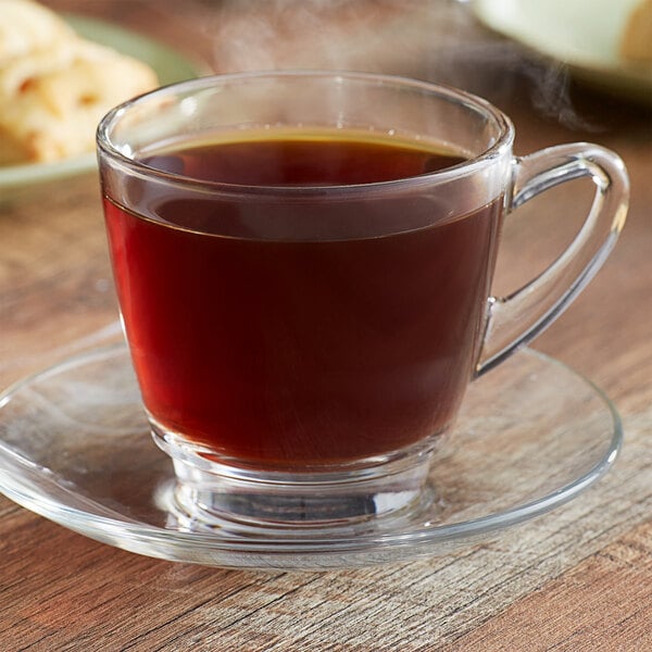 A glass cup of Ellis Colombian whole bean coffee on a saucer.