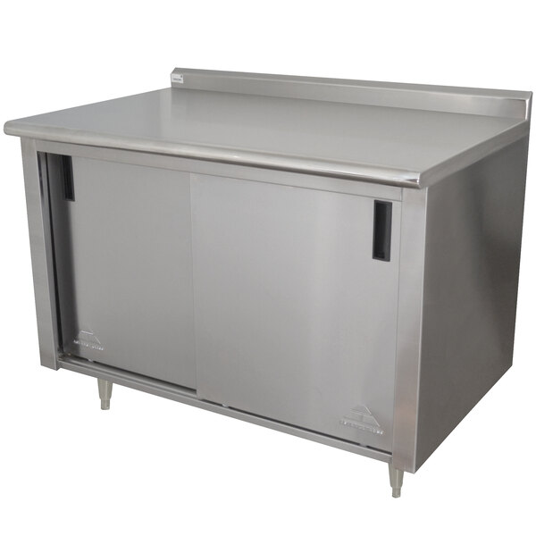A stainless steel Advance Tabco work table with cabinet doors and a mid shelf.