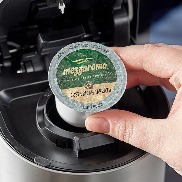 A hand holding an Ellis Mezzaroma Costa Rican Tarrazu coffee capsule over a coffee maker.