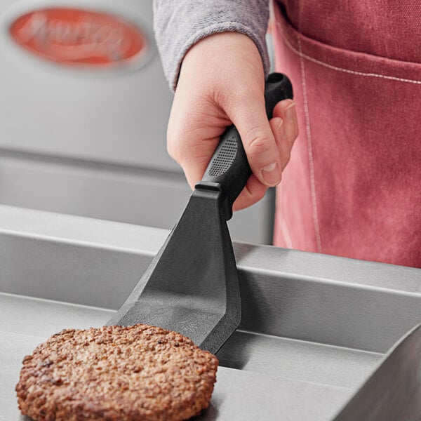 A person using a Fourt&#233; black nylon solid turner to flip a burger on a pan.