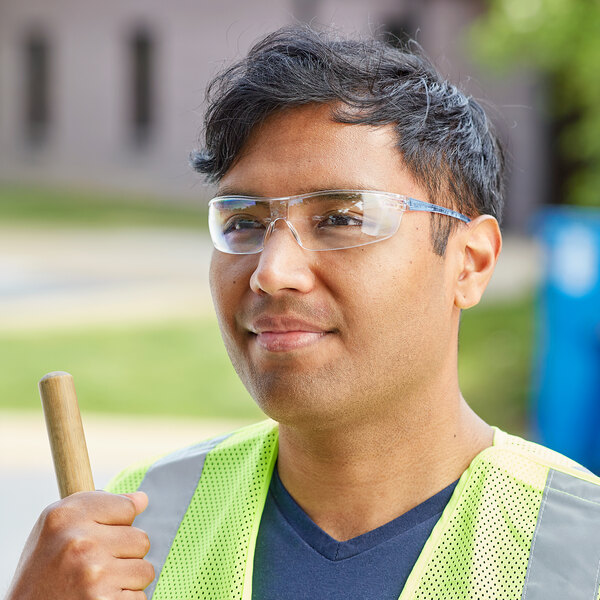 A man wearing Honeywell Uvex safety glasses and a reflective vest while holding a pipe.