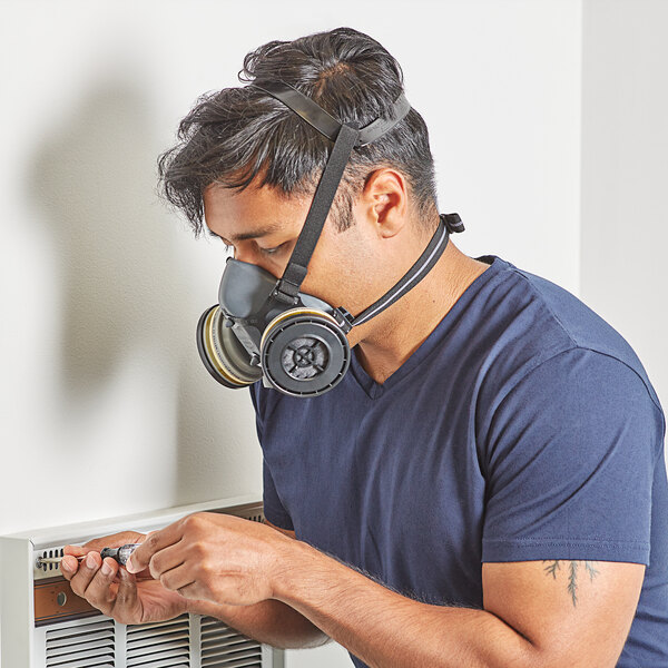 man wearing a half face respirator while performing maintenance on an air conditioner