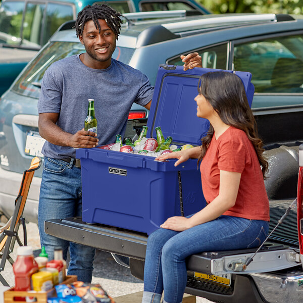 A man and woman sitting on the back of a truck with a CaterGator navy cooler.