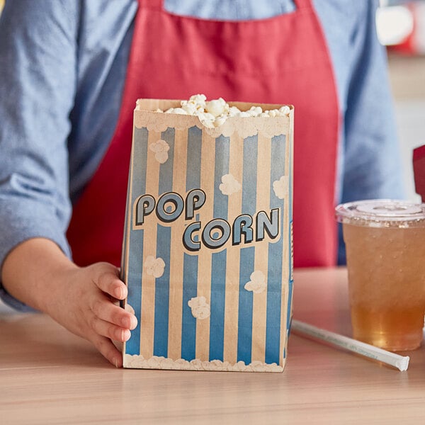 A hand holding a Bagcraft Packaging EcoCraft popcorn bag full of popcorn.