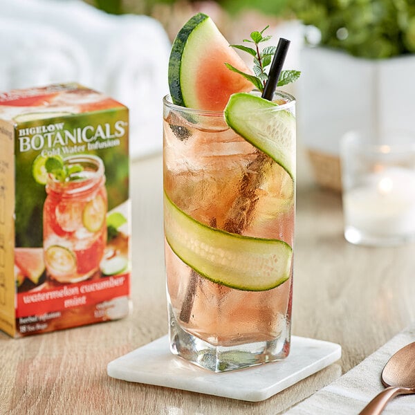 A glass of water with a cucumber slice and a slice of watermelon on the rim.