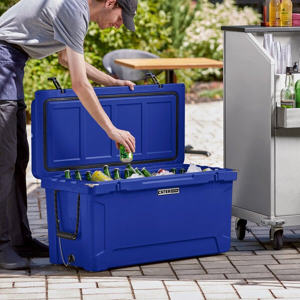 A man putting a bottle of beer into a navy CaterGator outdoor cooler.