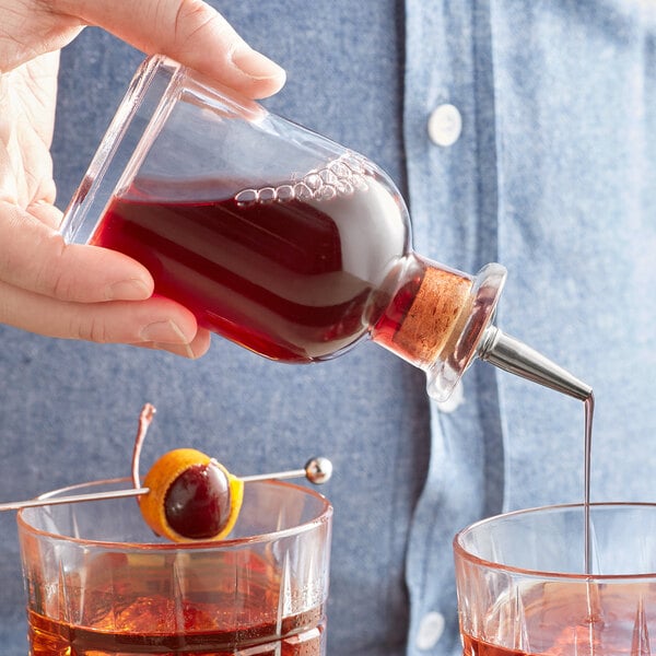 A person using an Arcoroc clear bitters bottle to pour liquid into two glasses.