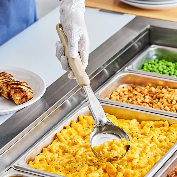 A hand holding a Vollrath Jacob's Pride Ivory Spoodle over macaroni and cheese.