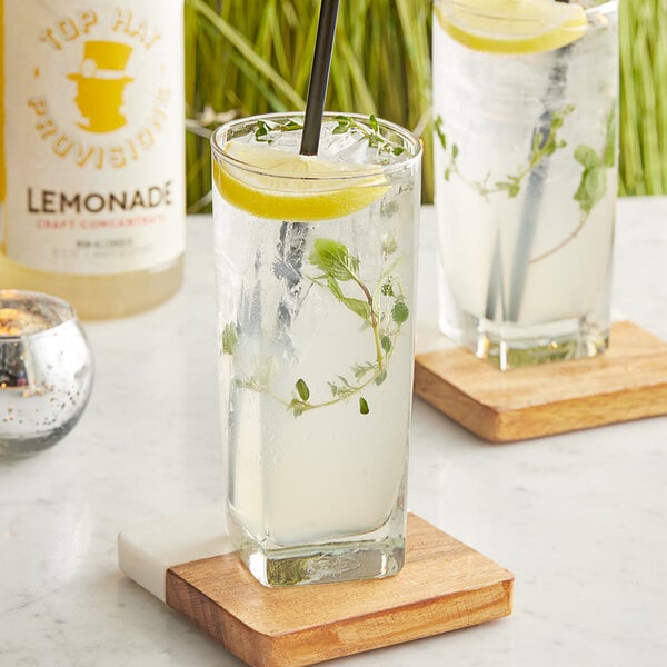 A glass of Top Hat Provisions Lemonade with a lemon slice and a straw on a coaster.