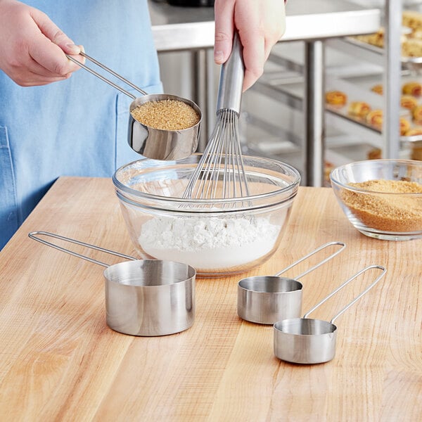 A person using American Metalcraft stainless steel measuring cups to mix brown powder in a bowl.