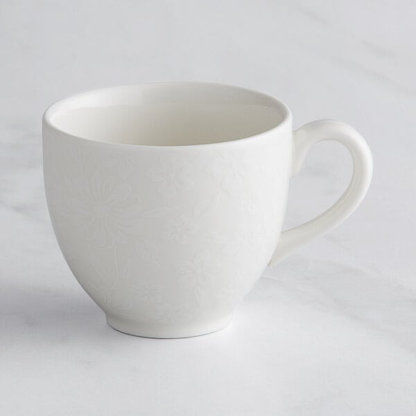 A close-up of a white RAK Porcelain cup with an embossed floral design.