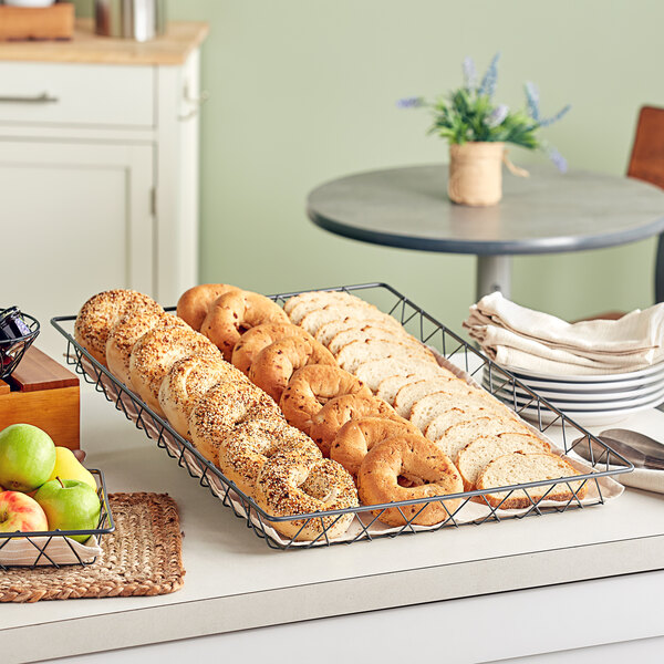 A rectangular wire basket with bagels inside on a bakery counter.