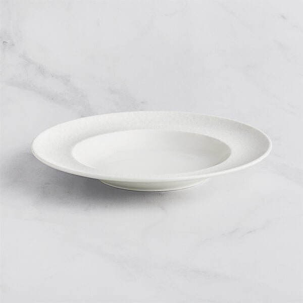 A RAK Porcelain ivory deep plate with an embossed rim on a marble surface.