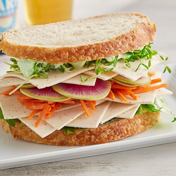 A sandwich with GOOD PLANeT Plant-Based Pepper Jack Cheese slices and vegetables on a plate.