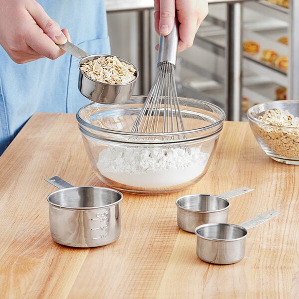 A person mixing oats and flour in a bowl with Tablecraft measuring cups and a whisk.