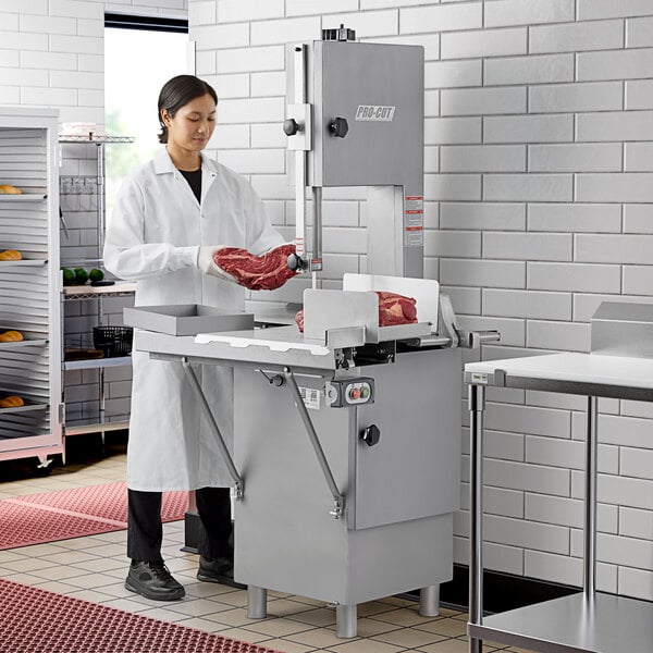 A woman in a white coat using a ProCut vertical band meat saw to cut meat.