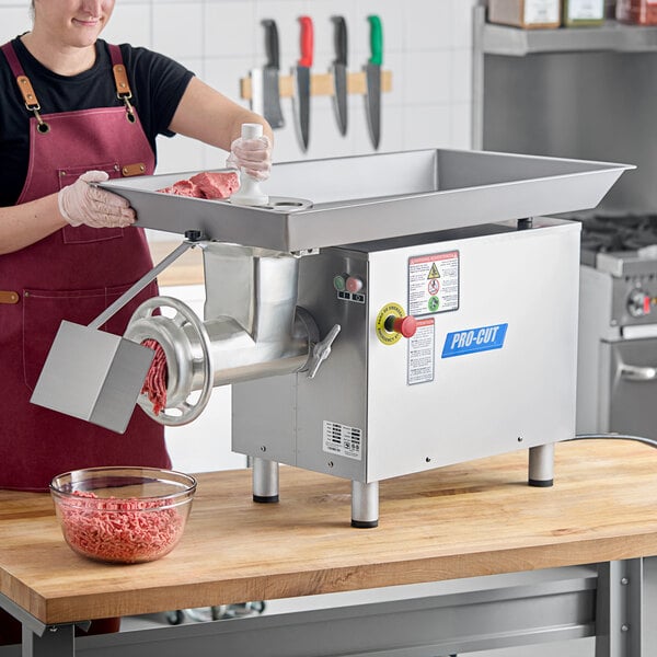 A woman in an apron using a ProCut #32 electric meat grinder on a counter in a butcher shop to grind meat.