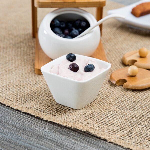 A white square porcelain sauce cup filled with yogurt and blueberries.